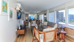 A modern living room with a sofa, chairs, a coffee table, and a TV. There is a dining area with a table and chairs in the background. - Ilikai Hotel, Amazing Ocean views! Most desirable location in Ilikai! (Honolulu)