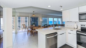 A modern kitchen with white cabinetry, a built-in oven, and a dining area with a table and chairs. - Ilikai Hotel, Amazing Ocean views! Most desirable location in Ilikai! (Honolulu)