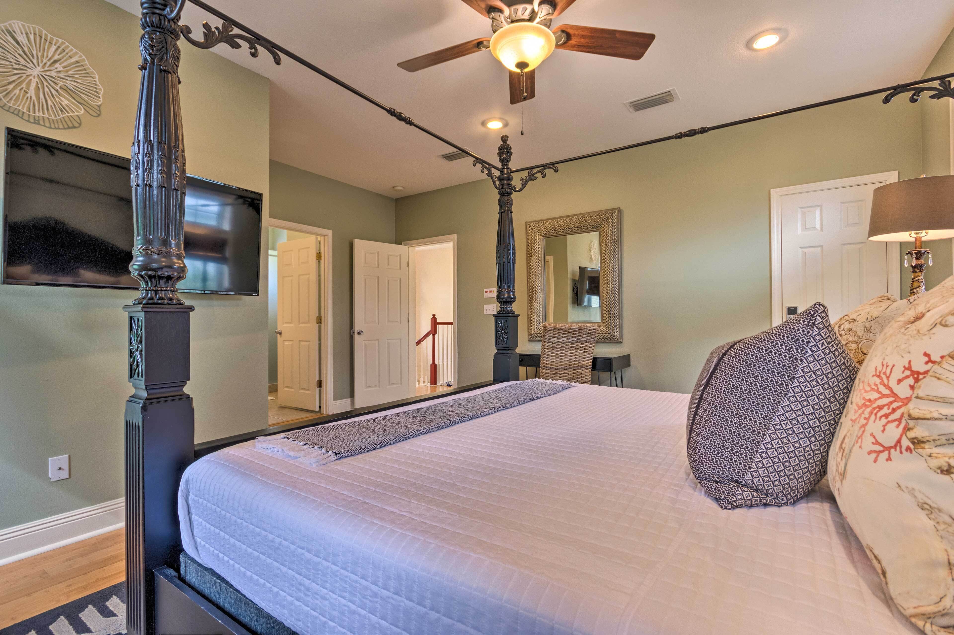 A bedroom with a large bed, a ceiling fan, a flat-screen TV, and a mirror.