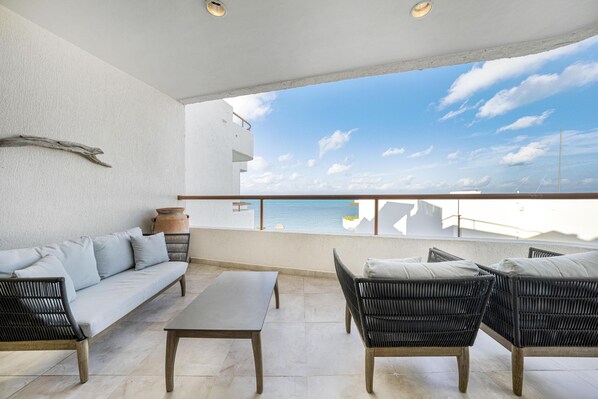 Un balcon avec un canapé, des chaises et une table, donnant sur une étendue d’eau et un ciel dégagé.