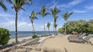 Un resort sulla spiaggia con palme, poltrone da relax e vista chiara sull'oceano.