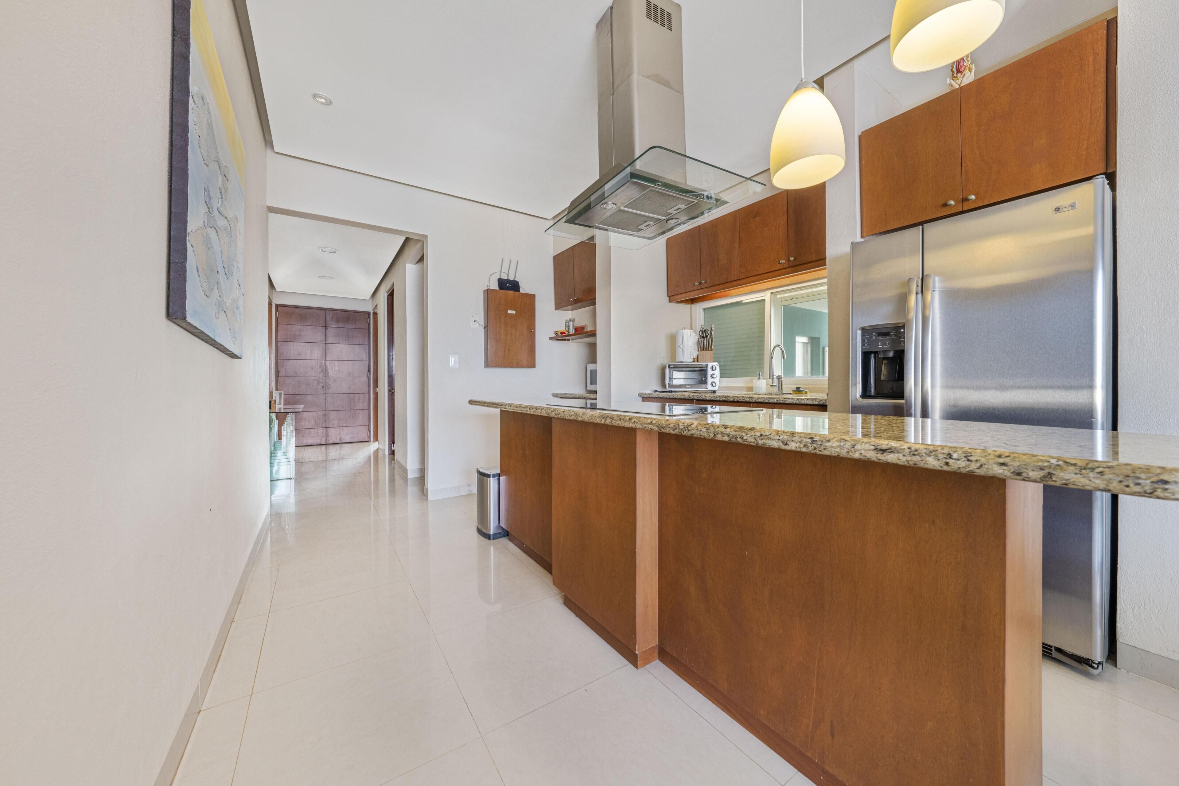 A modern kitchen with a central island, stainless steel appliances, wooden cabinets, and pendant lighting.