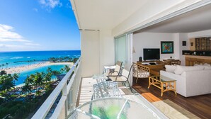 A balcony with a view of a beach and ocean, furnished with a sofa, chairs, and a glass table. - Great Ocean View At The Ilikai Hotel! (Honolulu)