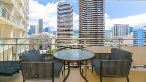 Un balcon avec une table ronde et quatre chaises en osier, d’où l’on peut admirer une vue sur la ville, avec ses nombreux immeubles.