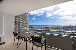 Ein Balkon mit Blick auf einen Yachthafen und das Meer, ein Tisch und Stühle.