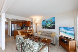 Un salon moderne avec un canapé, une table basse et un meuble pour la télévision, une cuisine avec des meubles en bois, et un coin repas avec des chaises et une table.
