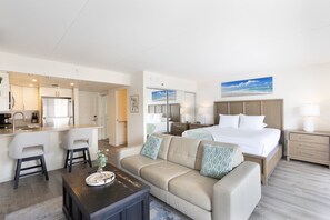 A hotel room with a bed, a sofa, a dining area, and a kitchen.