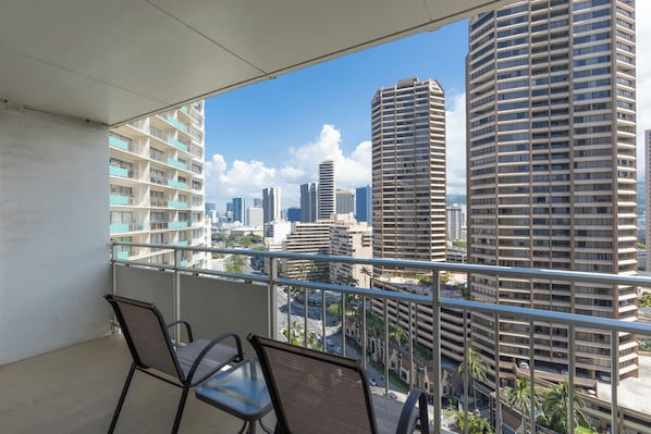 A balcony with two chairs and a table, overlooking a cityscape with tall buildings.