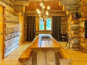 L’intérieur d’une cabane en rondins, avec une table à manger en bois, un lustre et une vue par la fenêtre.