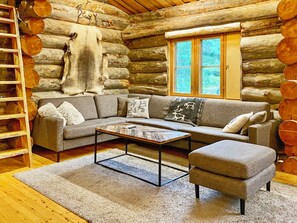 L'intérieur d'une cabane en rondins, avec un canapé, un pouf, une table basse et une fenêtre donnant sur la forêt.