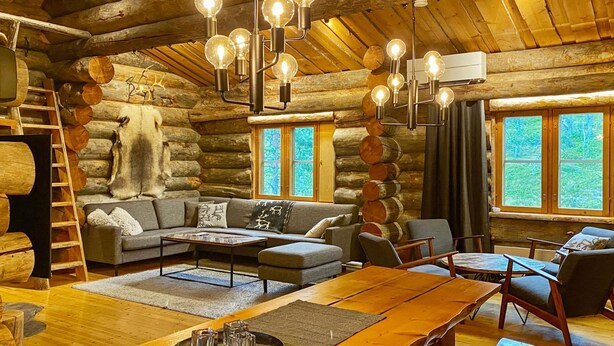 A log cabin interior with a wooden dining table, a sofa, and a chandelier.