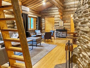 A log cabin interior with a wooden ladder, a fireplace, and a stone wall.
