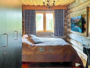 Une chambre dans une cabane en rondins, avec un lit, des rideaux, un tableau et un lustre.