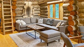 A log cabin interior with a sectional sofa, a coffee table, a ladder, and a large window.