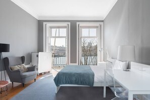 Une chambre d’hôtel moderne, équipée d’un lit, d’un bureau, d’une chaise et offrant une vue sur le paysage urbain grâce à de grandes fenêtres.