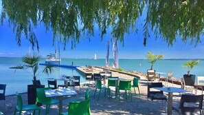 Een restaurant aan het strand met terras, een zwembad en uitzicht op zee en zeilboten.