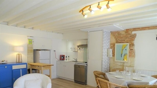 A compact living space with a kitchenette, dining area, and a white armchair.