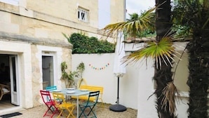 A small outdoor patio with a table and chairs, surrounded by a white wall and a palm tree.