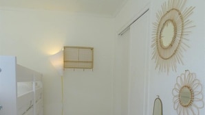 A small, white room with a bunk bed, a woven basket, and decorative wall art.