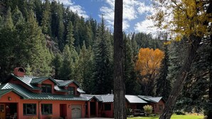 Eine Lodge mit roter Außenfassade und einem grünen Dach, umgeben von einem Wald mit herbstlich gefärbten Bäumen.