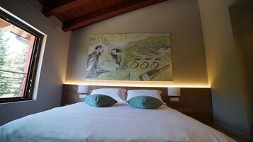 Un dormitorio con una cama grande, dos almohadas, una lámpara de pared y un cuadro sobre la cama.