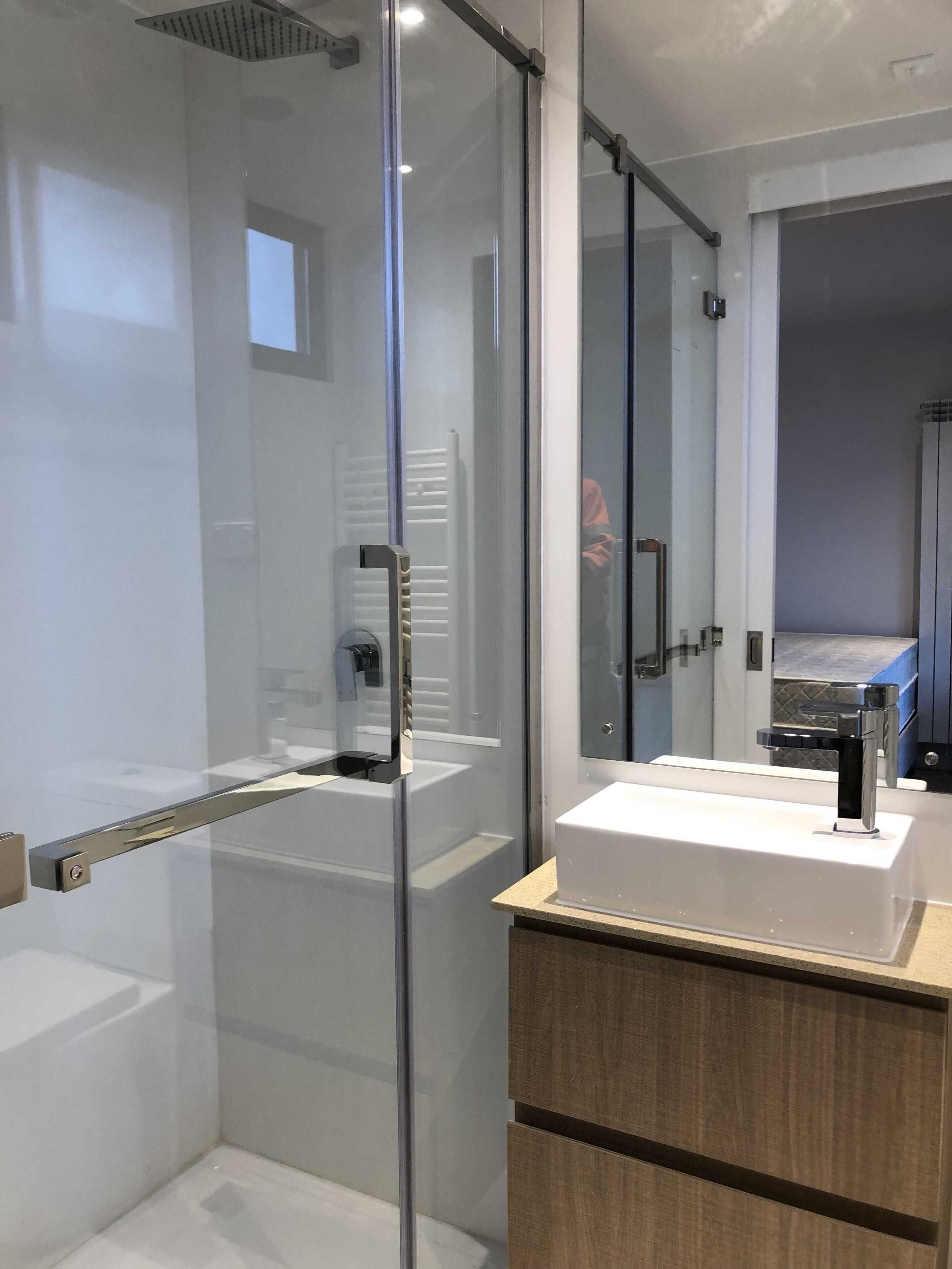 A modern bathroom with a glass shower enclosure, a white sink, and a wooden vanity.