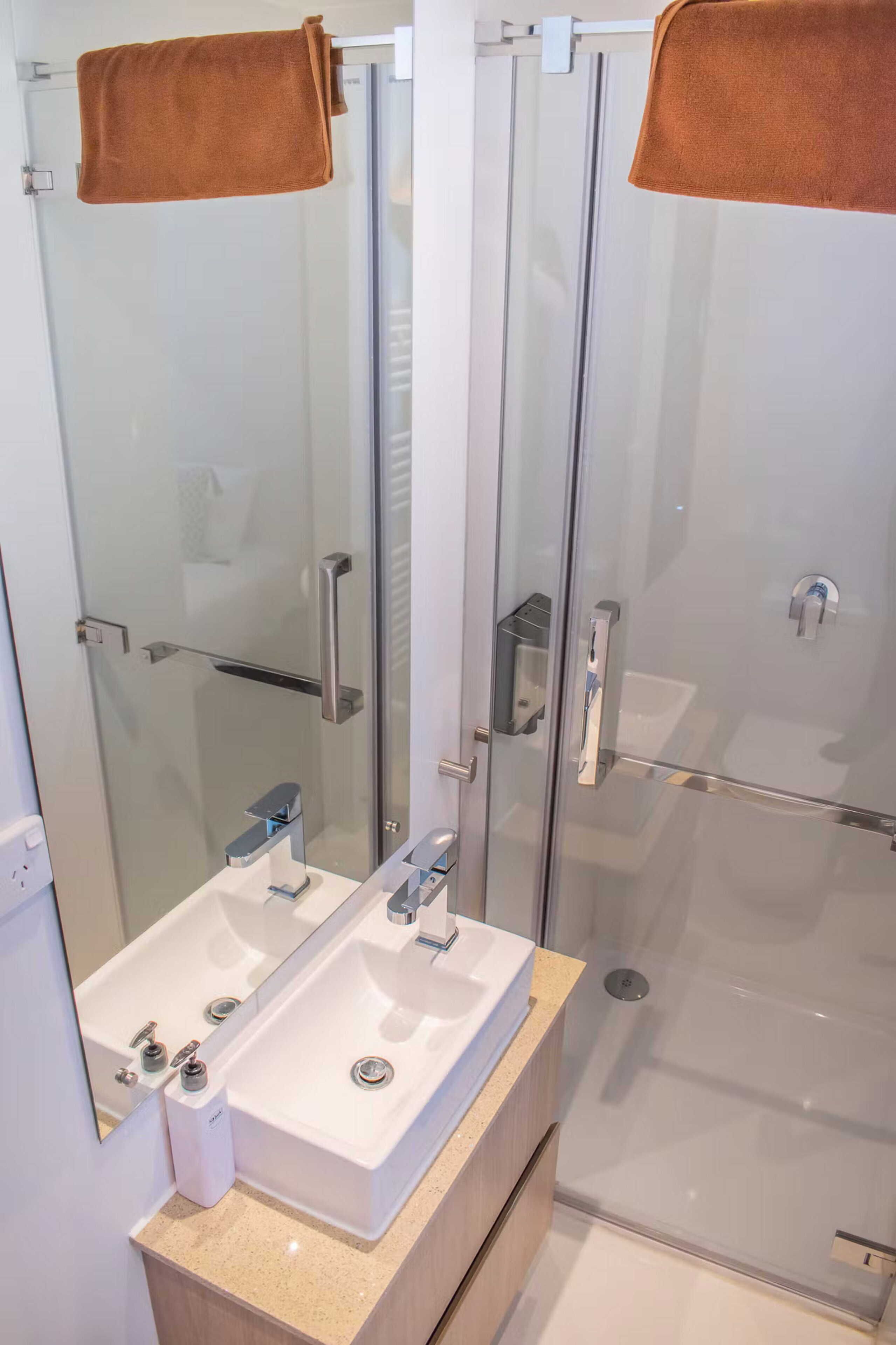 A modern bathroom with a glass shower enclosure, a double sink vanity, and a towel rack.