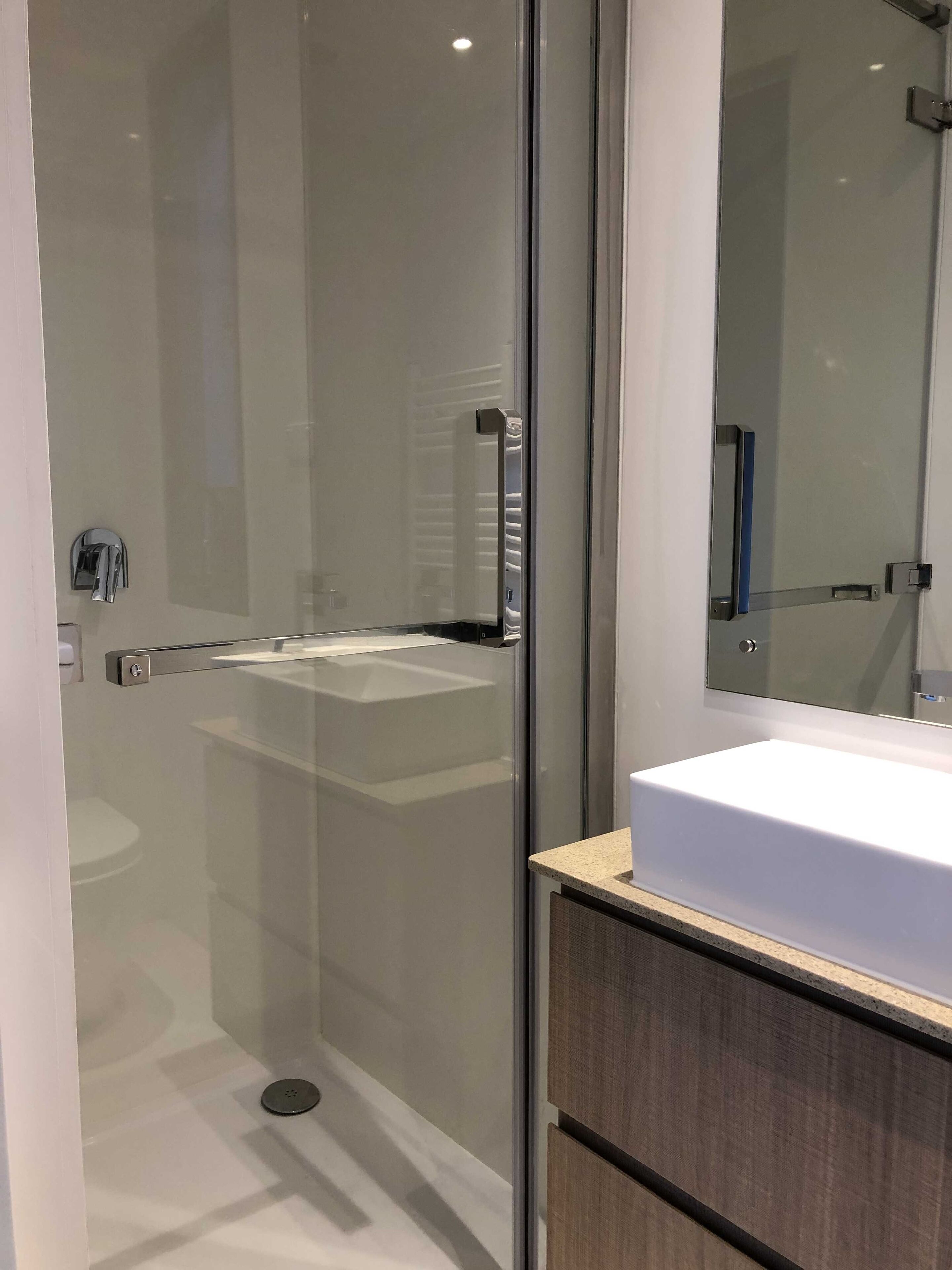 Un baño moderno con cabina de ducha de vidrio, un lavamanos blanco y un espejo.