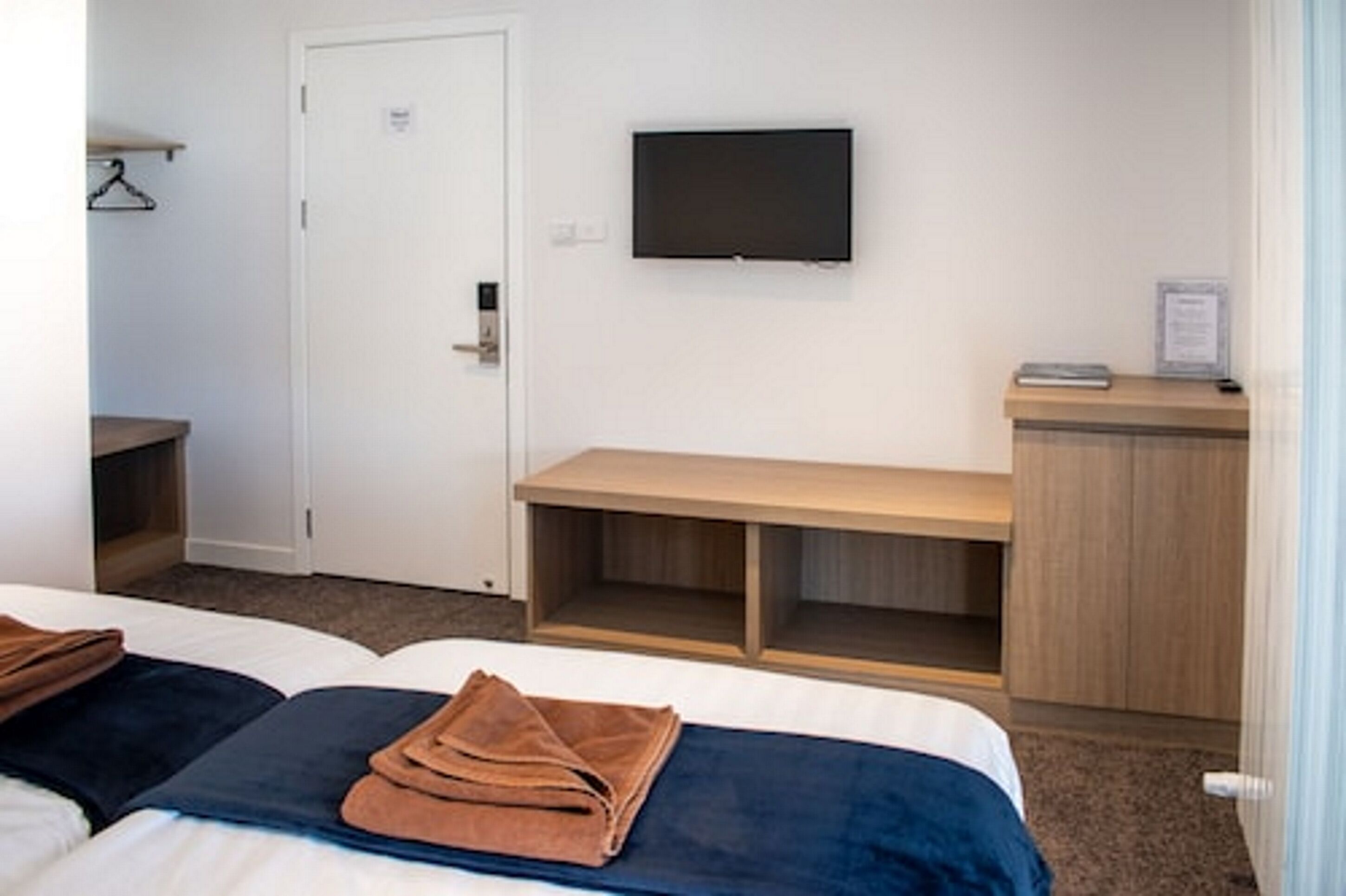 A hotel room with two beds, a TV mounted on the wall, a wooden desk, and a door with a handle.