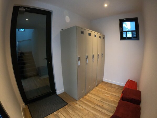 Una habitación con una puerta de vidrio corredera que da a una escalera, varios casilleros y un televisor pequeño montado en la pared.