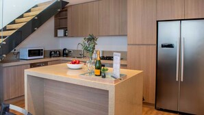 Una cocina moderna con una isla central, electrodomésticos de acero inoxidable y una escalera de madera.