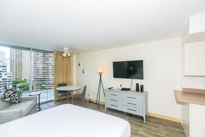 Een hotelkamer met een bed, bureau, stoel, televisie en uitzicht op hoge gebouwen.