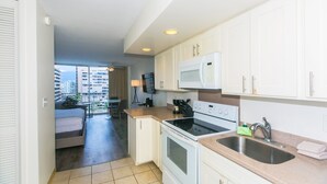 Une cuisine moderne avec des meubles blancs, un four à micro-ondes, une cuisinière et un évier. Un balcon offre une vue sur les immebles.