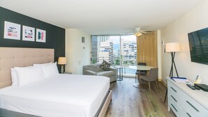 Une chambre d’hôtel équipée d’un lit, d’un bureau, d’une chaise et d’un balcon offrant une vue sur les bâtiments.