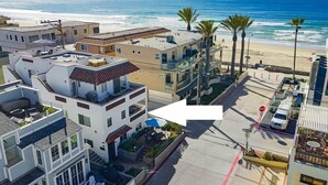 Un edificio residencial de varios pisos con terraza en la azotea, vista al mar y zona de estacionamiento con una señal de parada.