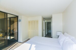 A hotel room with a bed, a desk, and a chair. There is a sliding door leading to another room. - Great Location In Wakiki, Walking Distance To Beach, Shopping, Dining! (Honolulu)