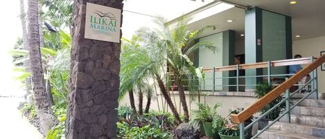 A stone pillar with a sign reading "ILIKAI MARINA" in a lobby area with a staircase, palm trees, and indoor plants.