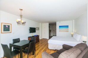Une chambre d’hôtel comprenant un lit, un bureau avec une chaise, une table à manger avec des chaises, un téléviseur et un lustre.
