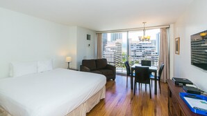 A hotel room with a large bed, a desk with a chair, and a view of tall buildings. - Full Kitchen, Studio, Just Minutes to the Beach! (Honolulu)