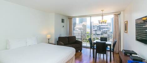 A hotel room with a large bed, a desk with a chair, and a view of tall buildings.