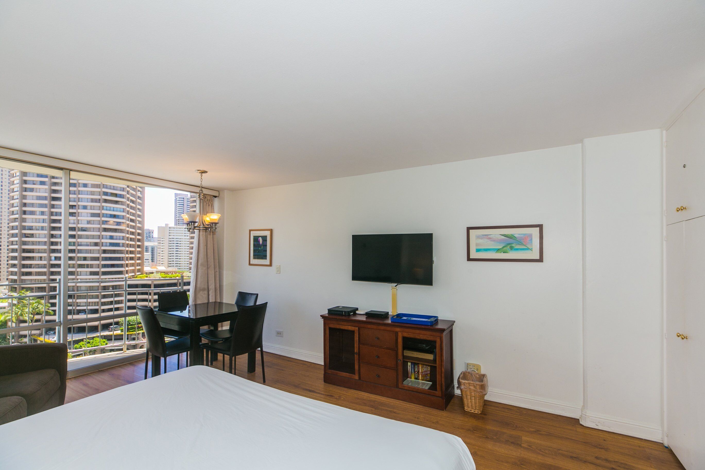 A hotel room with a large bed, a desk with a chair, a TV, and a view of tall buildings.