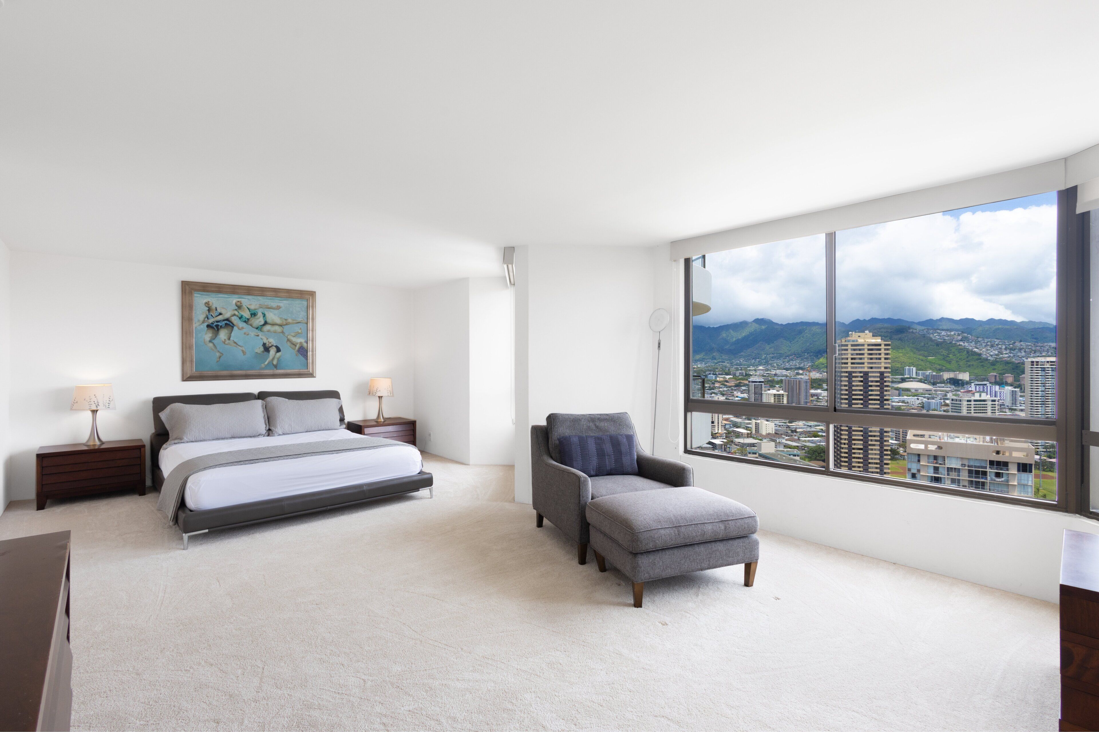A bedroom with a bed, a chair, a nightstand, a painting, and a large window with a city view.