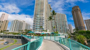 A high-rise hotel with multiple floors, a pedestrian bridge, and palm trees. - Cozy 14th floor condo overlooking the surrounding Waikiki area!  Great price! (Honolulu)