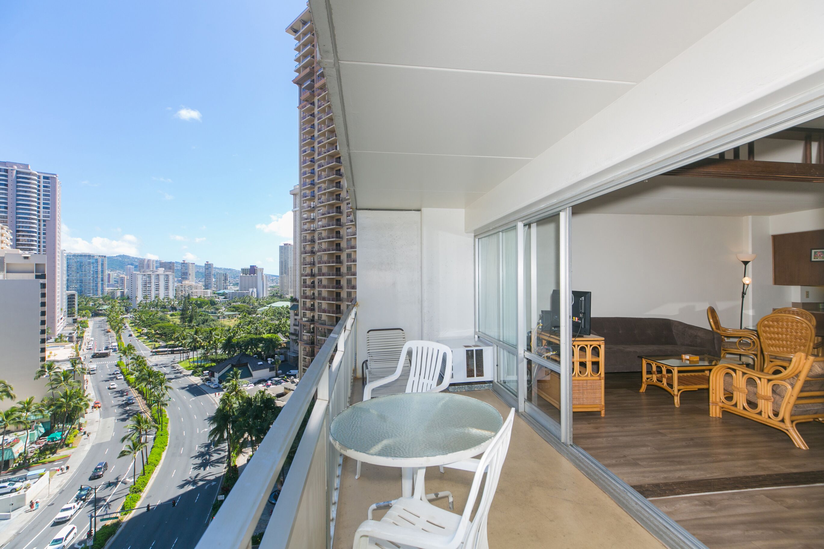 Uma varanda com mesa e cadeiras de vidro, um sofá e uma televisão.