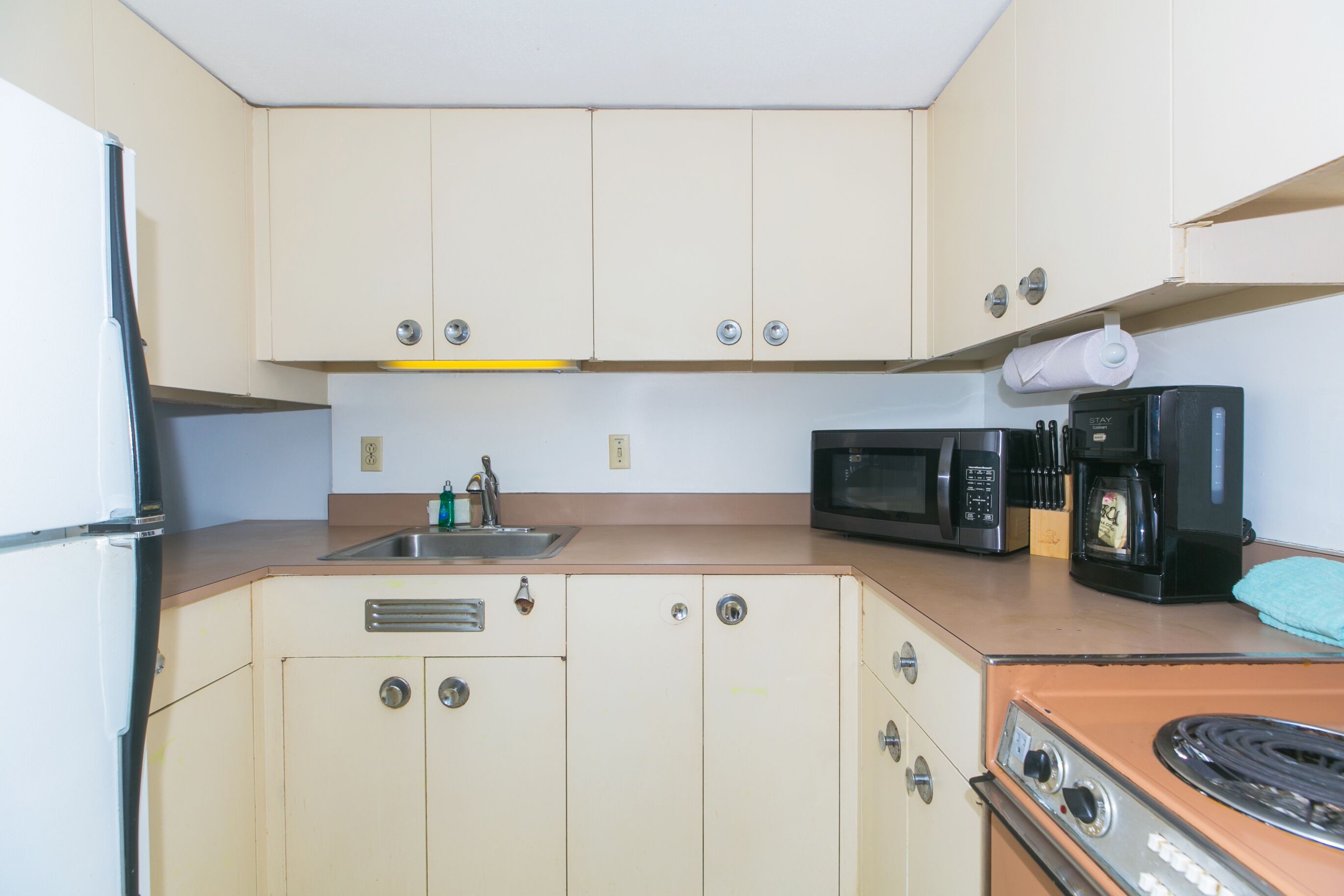 Una kitchenette compacta con refrigerador, microondas, cafetera y estufa.