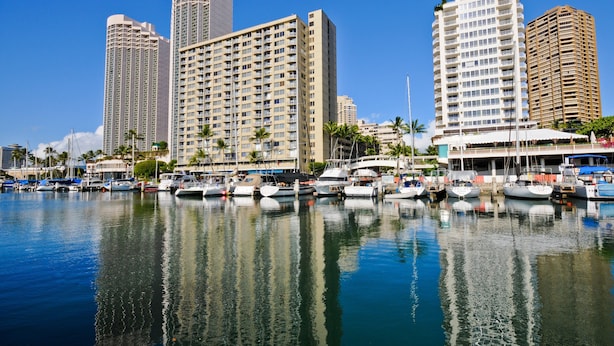 Un port de plaisance où sont amarrés plusieurs bateaux, entouré d’immeubles de grande hauteur.