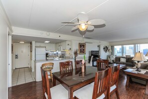 Cozinha moderna com armários brancos, sala de jantar com mesa e cadeiras de madeira e um ventilador de teto.