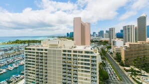Un hotel moderno de gran altura con varios balcones, una marina llena de barcos y un horizonte urbano de fondo.