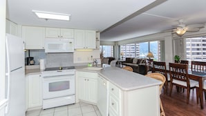Una cocina con armarios blancos, una estufa y un comedor con sillas de madera y una mesa.