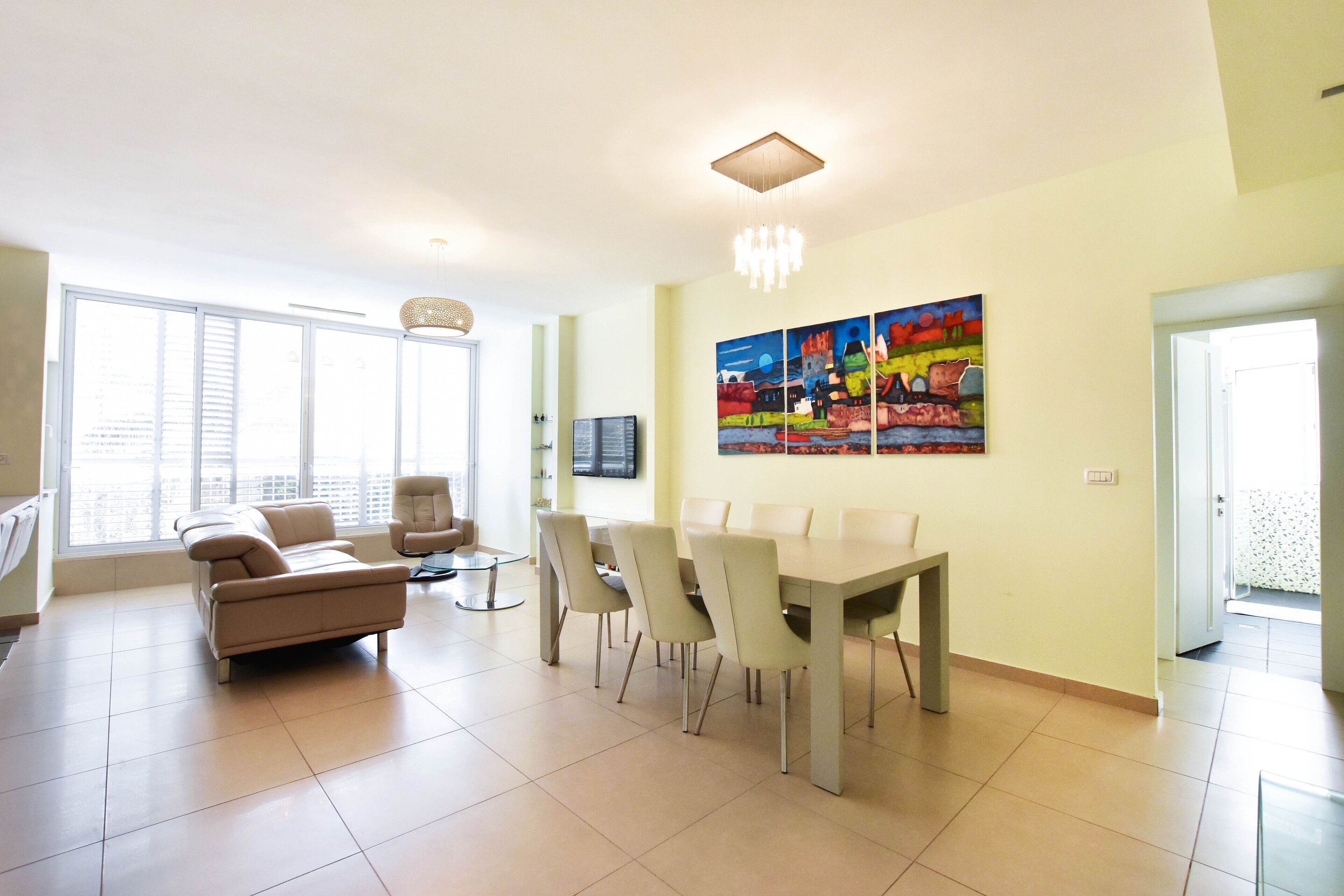 A modern living room with a sofa, chairs, a dining table, and a large window.